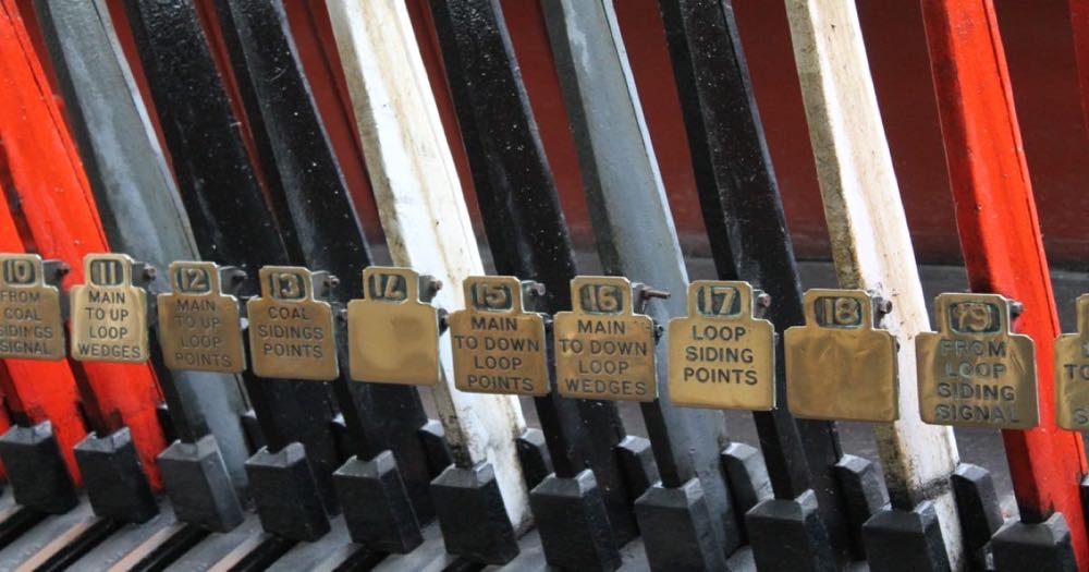 Rows of iron signal levers inside a Victorian railway signal box — each lever routes a train through the network, not for the operator's benefit but for everyone else's