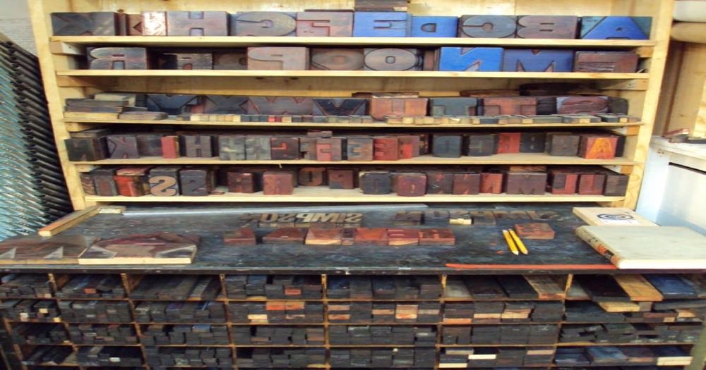 Rows of wooden letterpress type sorted into a compositor's tray, each character ready to be arranged into words — the physical act of choosing letters that make up a name