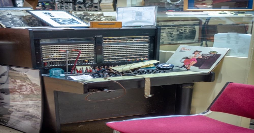 A vintage telephone operator's switchboard booth with rows of patch plugs and cables — a workspace built for relaying messages, waiting for the next call